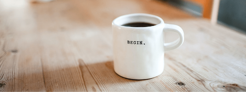 A cofee mug sits on a table with the word begin on it